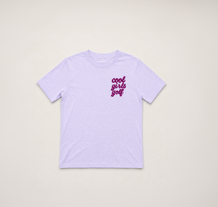 A light purple short-sleeve t-shirt with 'cool girls golf' printed in a dark purple cursive font on the left chest, displayed flat against a light beige background.