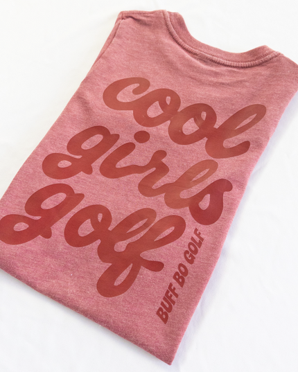 Folded pink t-shirt with 'cool girls golf' text on a white background