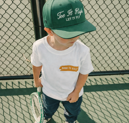 Child wearing a green cap and white t-shirt on a tennis court