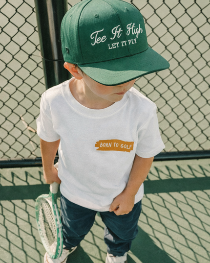 Child wearing a green cap and white t-shirt on a tennis court