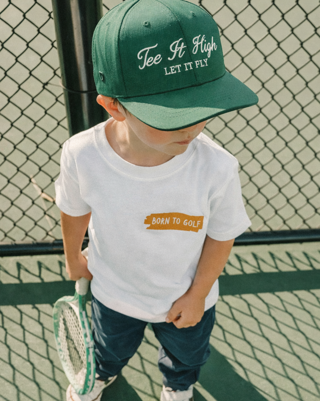 Child wearing a green cap and white t-shirt on a tennis court