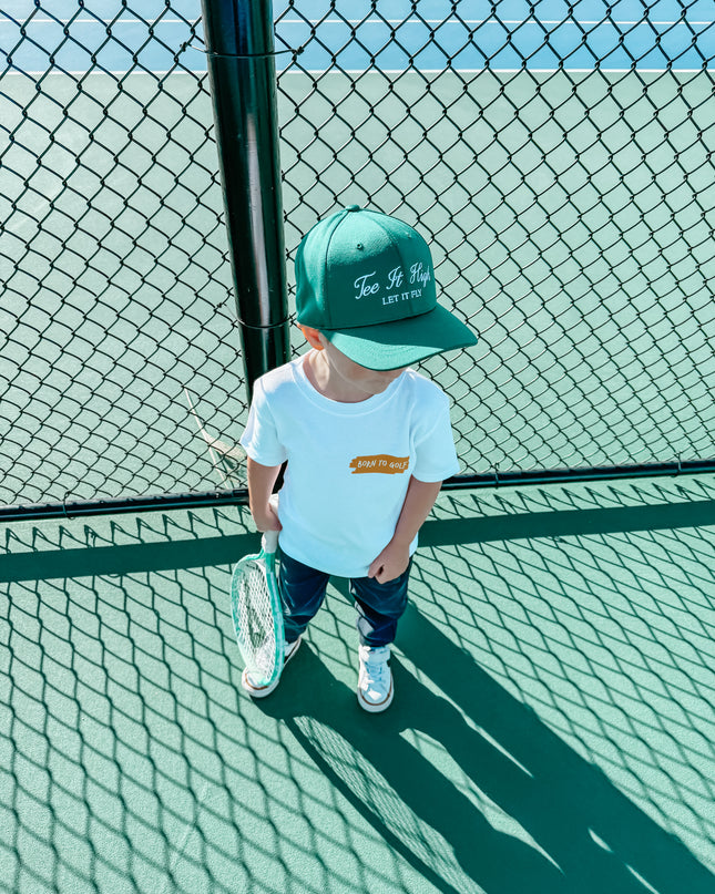 Child wearing a green cap and white shirt on a tennis court