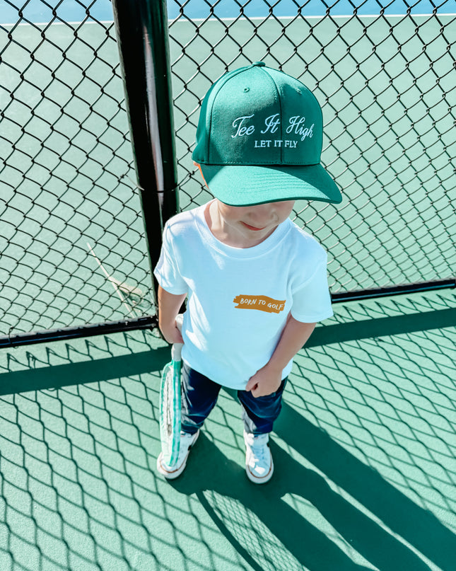 Child wearing a green cap and white t-shirt on a tennis court