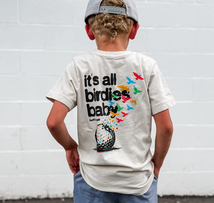 Child wearing a t-shirt with a golf-themed design against a white wall.