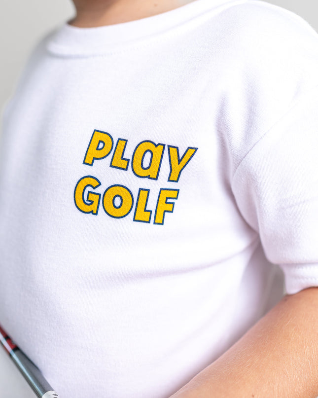 A close-up of a child wearing a white short-sleeve t-shirt with 'PLAY GOLF' printed in yellow and blue bubble letters on the chest, holding a golf club against a light gray background.