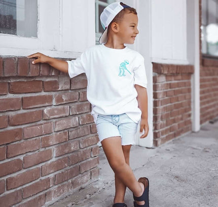 Child wearing a white t-shirt with a graphic design, standing against a brick wall.