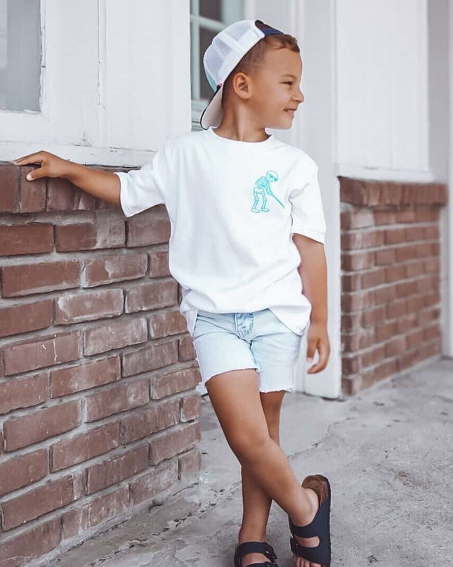 Child wearing a white t-shirt with a graphic design, standing against a brick wall.