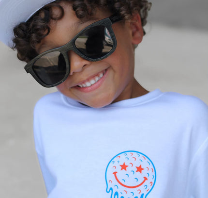 Child wearing a white cap and sunglasses with a shirt featuring a smiley face design.