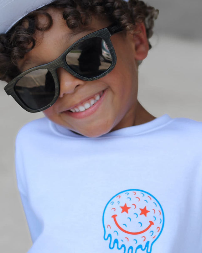 Child wearing a white cap and sunglasses with a shirt featuring a smiley face design.