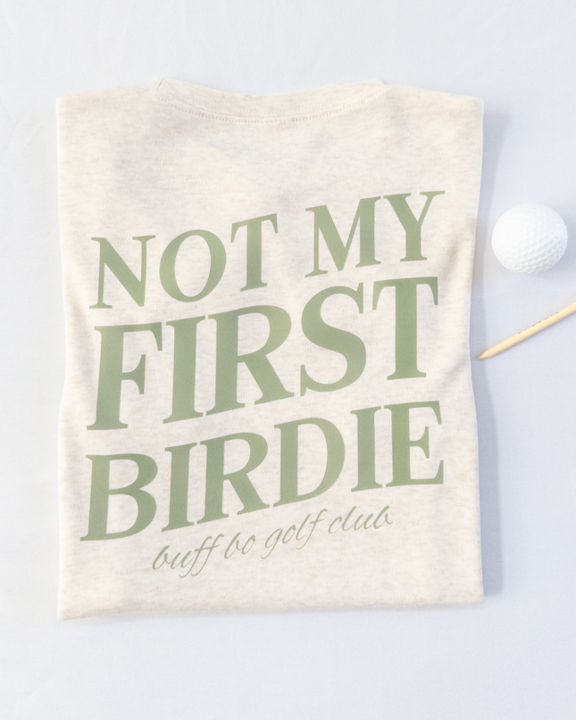 Beige towel with green text 'Not My First Birdie' on a light gray background