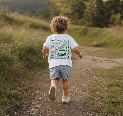 Child walking on a dirt path in a natural setting with a t-shirt featuring text and graphics.