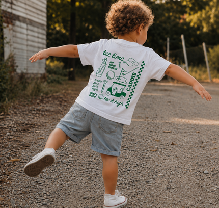 Child running on a road wearing a white t-shirt with green graphics and text.
