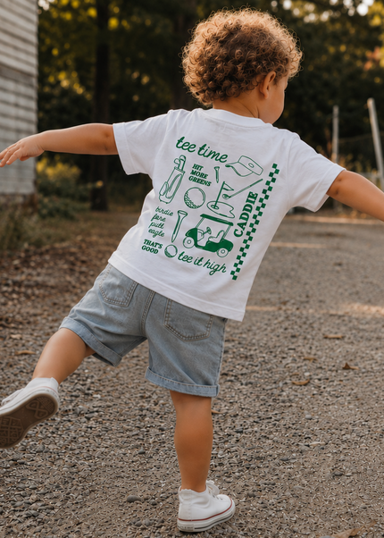 Child running on a road wearing a white t-shirt with green graphics and text.