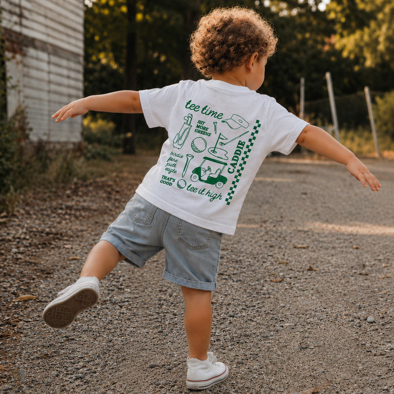 Child running on a road wearing a white t-shirt with green graphics and text.