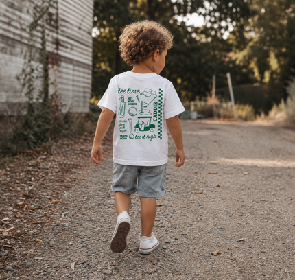 Child walking outdoors wearing a white t-shirt with graphics and text.