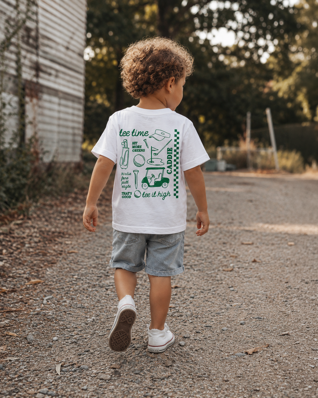 Child walking outdoors wearing a white t-shirt with graphics and text.