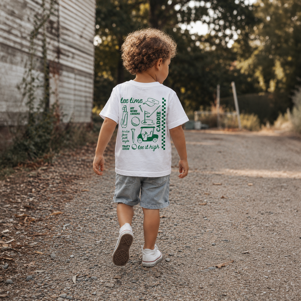 Child walking outdoors wearing a white t-shirt with graphics and text.