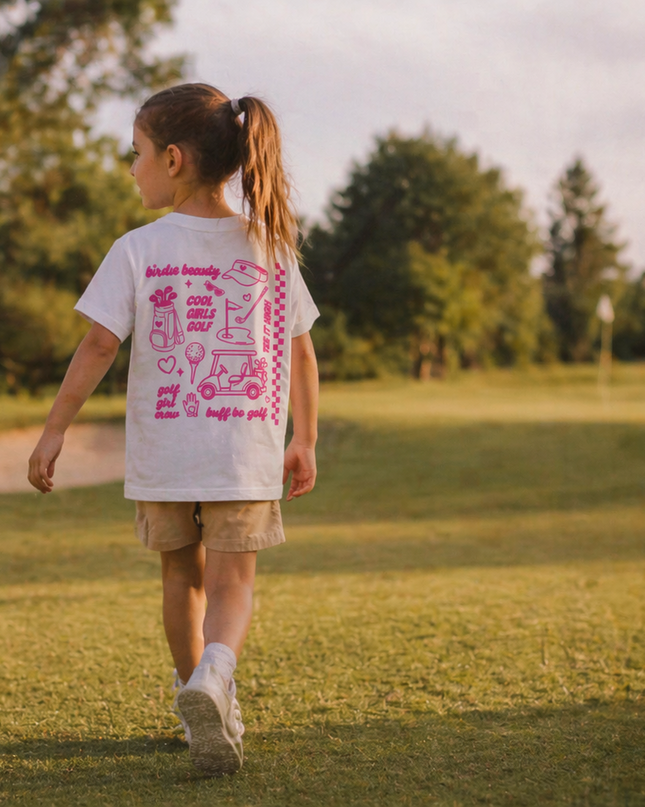 Child walking on a grassy field wearing a white t-shirt with pink graphics