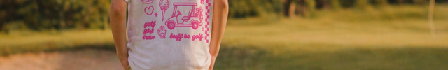 Young girl walking on a golf course wearing a white t-shirt with pink text and graphics.