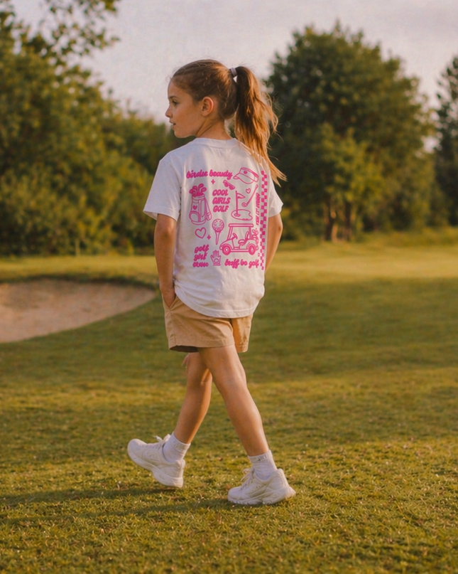 Person walking on a golf course wearing a white t-shirt with pink text and beige shorts.