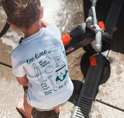 Child wearing a t-shirt with text and graphics, standing near a vehicle.