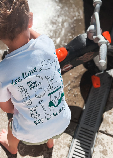 Child wearing a t-shirt with text and graphics, standing near a vehicle.