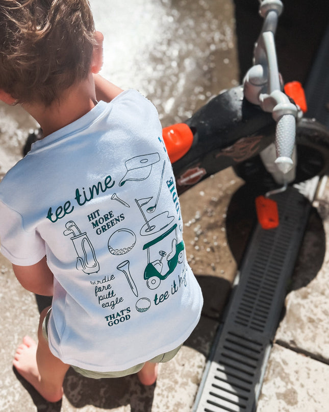 Child wearing a t-shirt with text and graphics, standing near a vehicle.