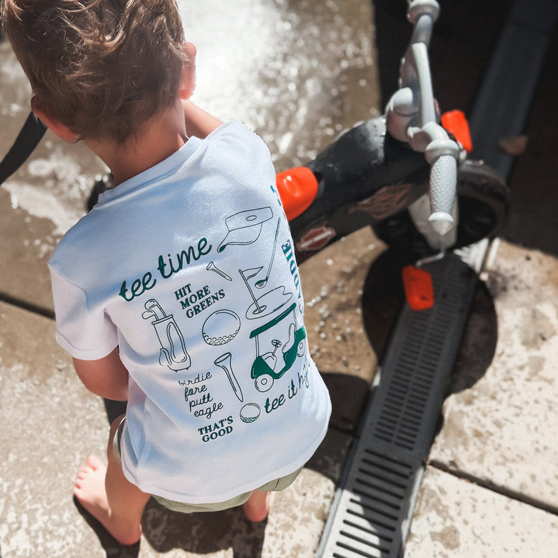 Child wearing a t-shirt with text and graphics, standing near a vehicle.