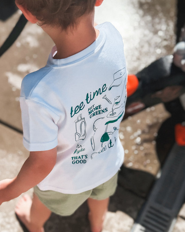 Child wearing a light blue and white t-shirt with text and graphics, standing on a sidewalk.