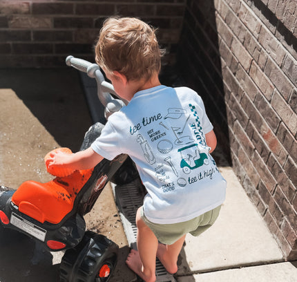 Child playing with a toy lawn mower on a concrete surface next to a brick wall.