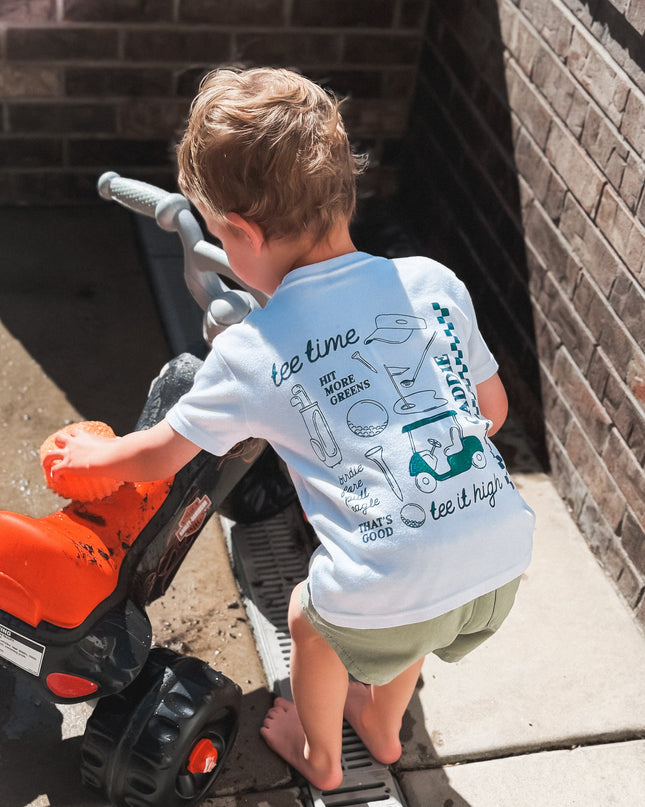 Child playing with a toy lawn mower on a concrete surface next to a brick wall.