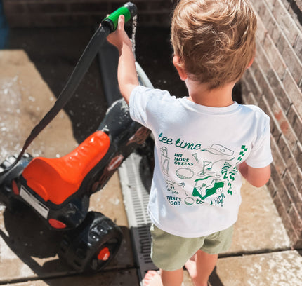 Child wearing a t-shirt with graphics and text, standing next to a lawn mower.