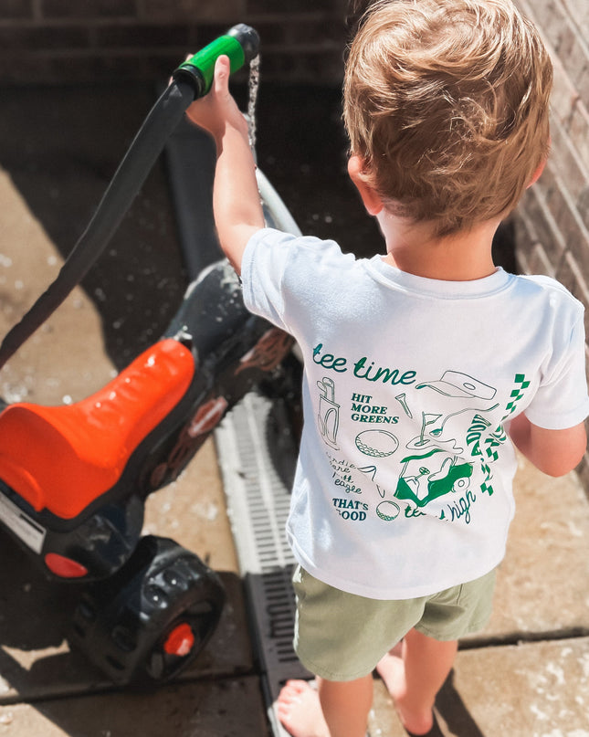 Child wearing a t-shirt with graphics and text, standing next to a lawn mower.