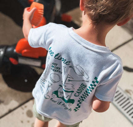 Child wearing a t-shirt with text and graphics, standing next to a toy bike.