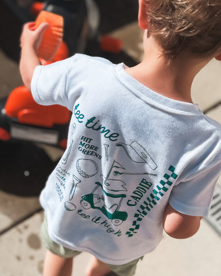 Child wearing a t-shirt with text and graphics, standing next to a toy bike.