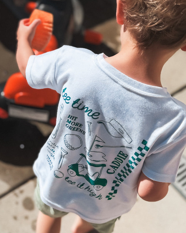Child wearing a t-shirt with text and graphics, standing next to a toy bike.