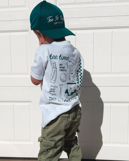 Child wearing a cap, t-shirt, and pants standing in front of a white garage door.