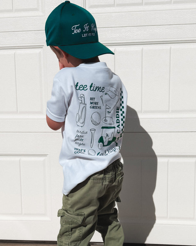 Child wearing a cap, t-shirt, and pants standing in front of a white garage door.