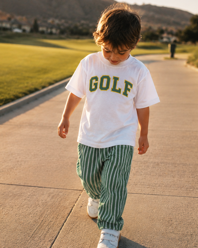Child wearing a 'GOLF' t-shirt walking on a path with mountains in the background