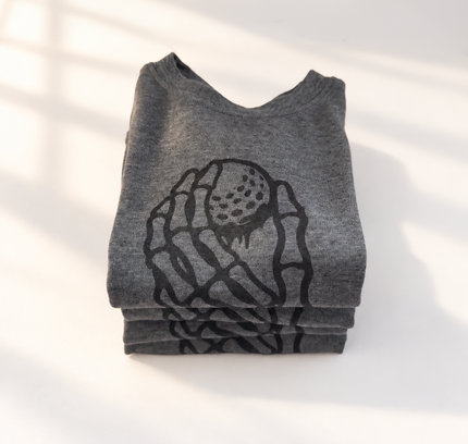 A folded heather gray t-shirt with a black graphic print of a hand holding a strawberry, photographed on a white surface with soft window shadows.
