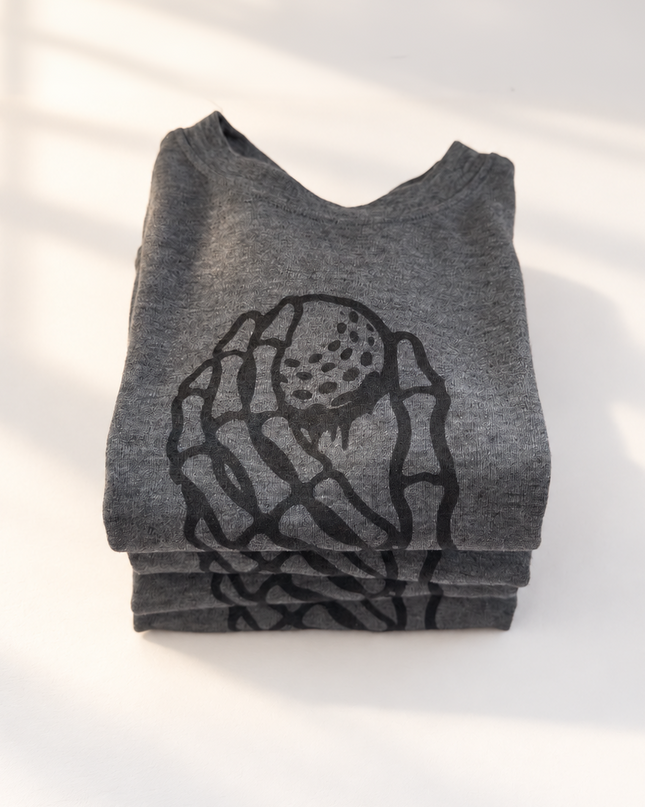 A folded heather gray t-shirt with a black graphic print of a hand holding a strawberry, photographed on a white surface with soft window shadows.