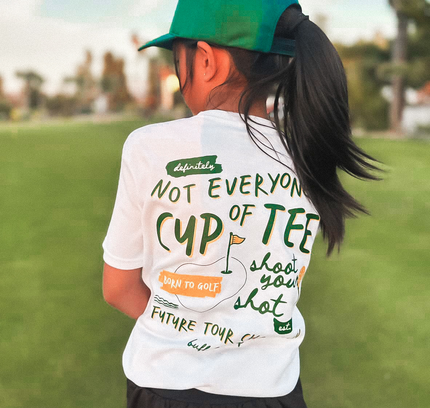 Person wearing a white t-shirt with text and a green cap on a grassy field.