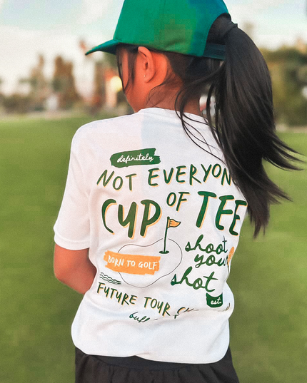 Person wearing a white t-shirt with text and a green cap on a grassy field.