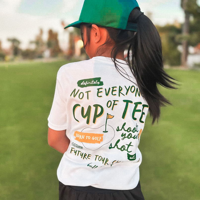 Person wearing a white t-shirt with text and a green cap on a grassy field.