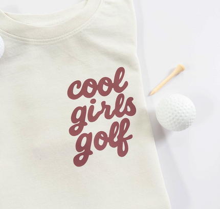 Folded white t-shirt with 'cool girls golf' text on a light background