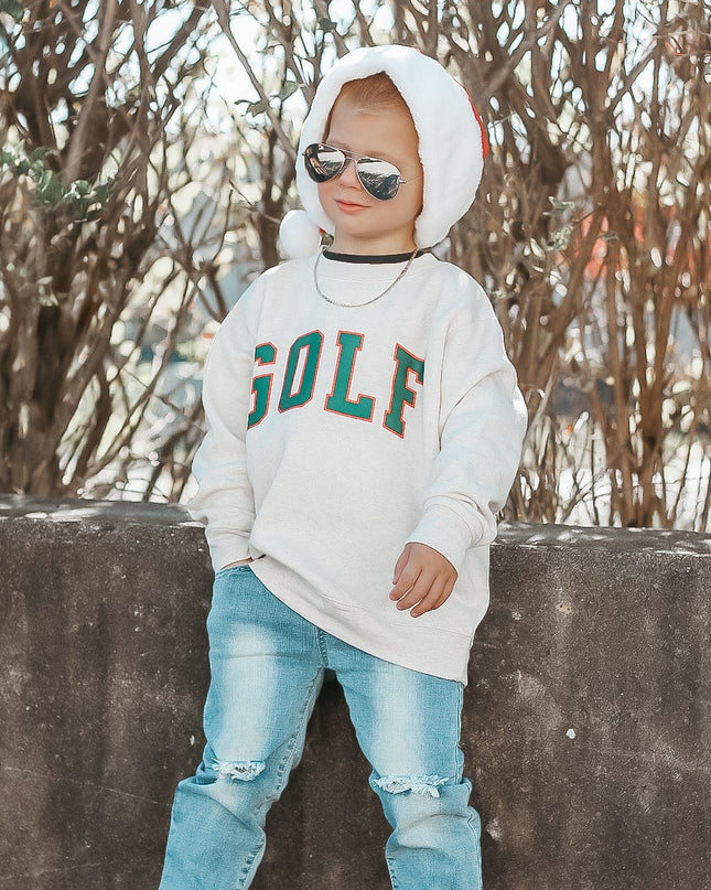 Child wearing a 'GOLF' sweatshirt, sunglasses, and ripped jeans against a natural background.