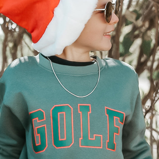 Person wearing a green 'GOLF' sweatshirt and Santa hat outdoors.