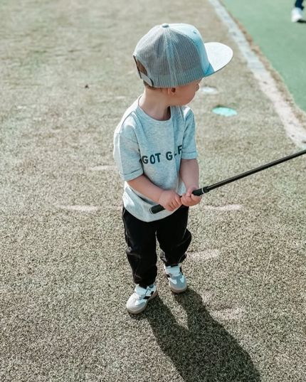 A stylish young golfer wearing a Buff Bo Outfitters 'Got Golf' shirt and snapback hat, practicing on the course. Perfect apparel for kids who love golf and quality design.