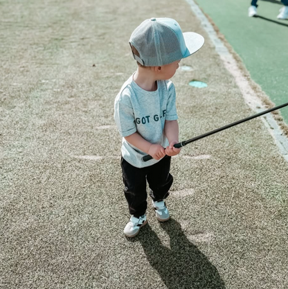 A stylish young golfer wearing a Buff Bo Outfitters 'Got Golf' shirt and snapback hat, practicing on the course. Perfect apparel for kids who love golf and quality design.