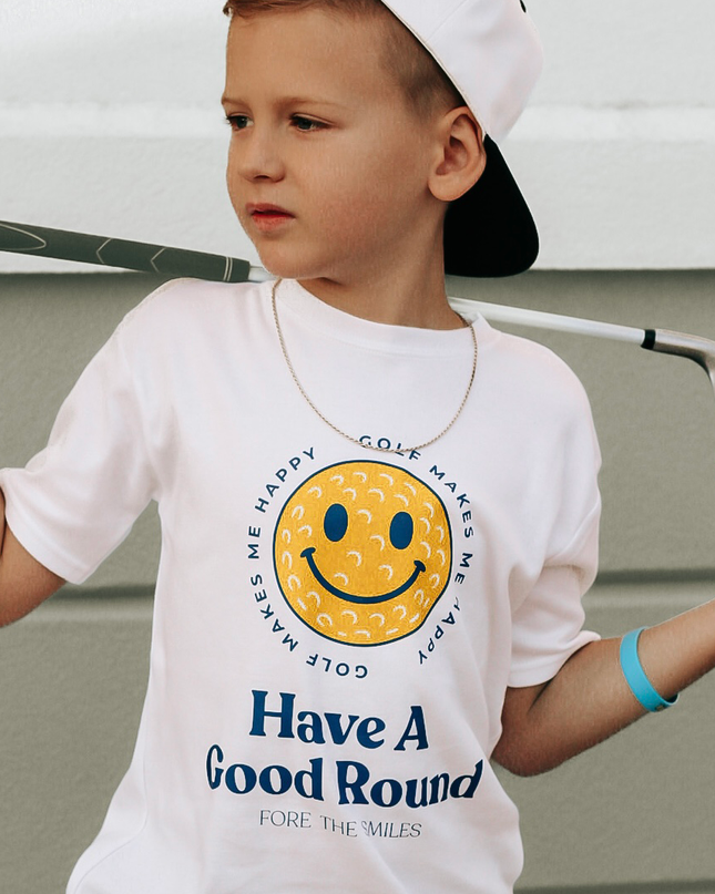 Child wearing a white t-shirt with a smiley face and text, holding a golf club.